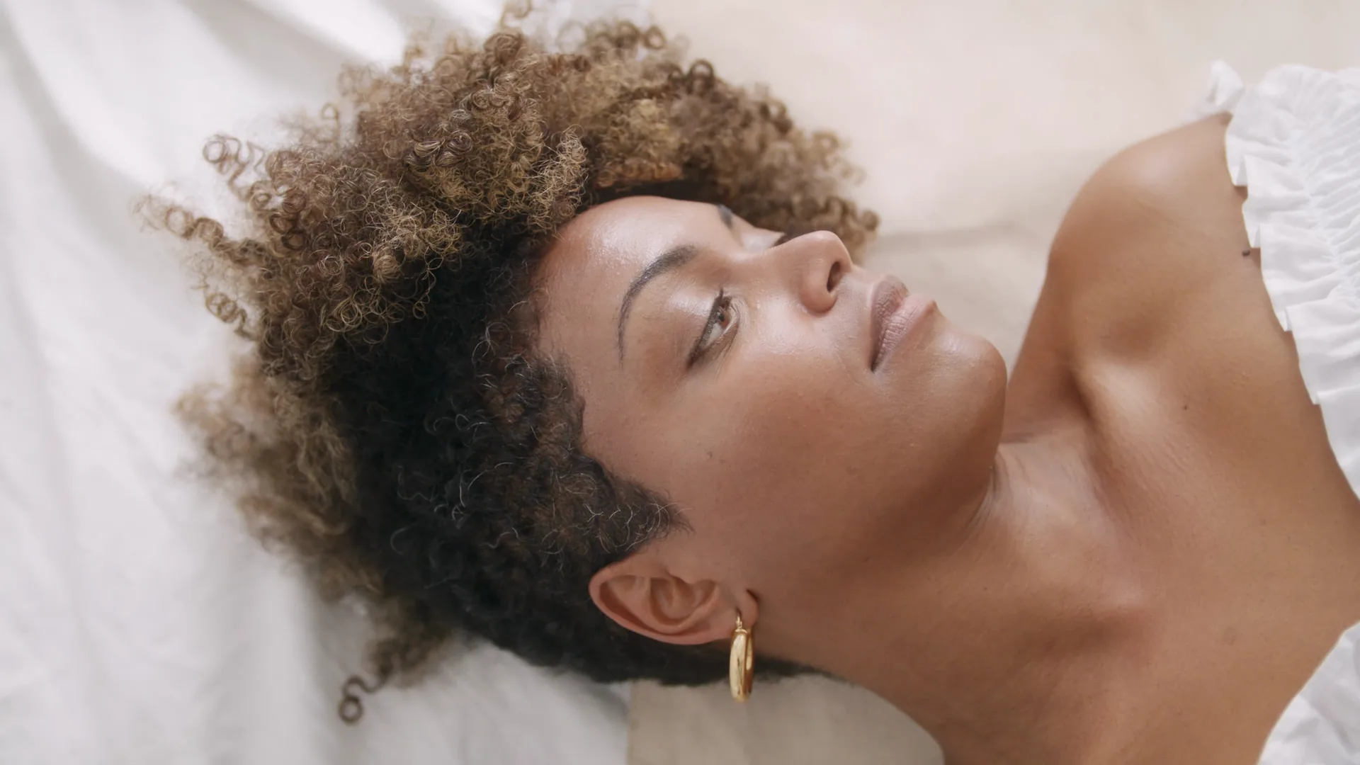 Woman lying back on white linen, eyes closed