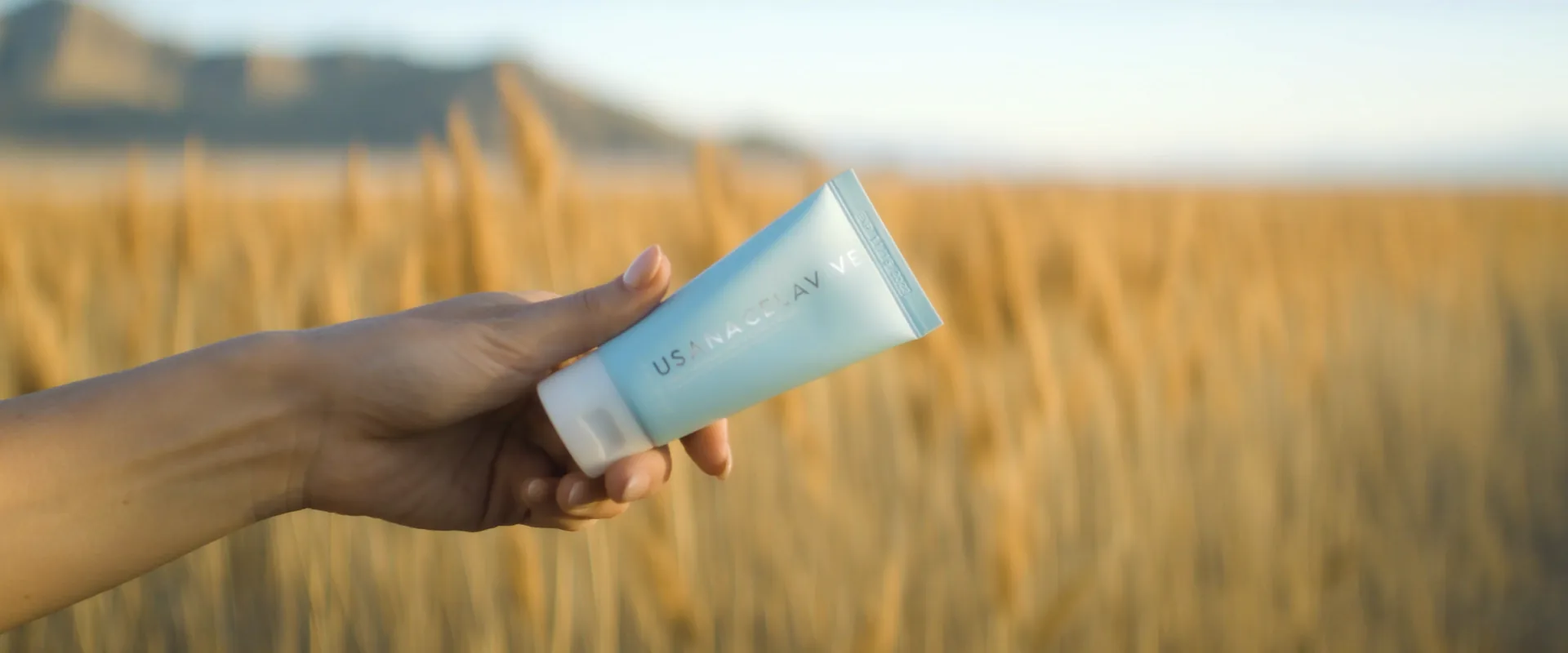 Hand holding the sunscreen tube against golden grass