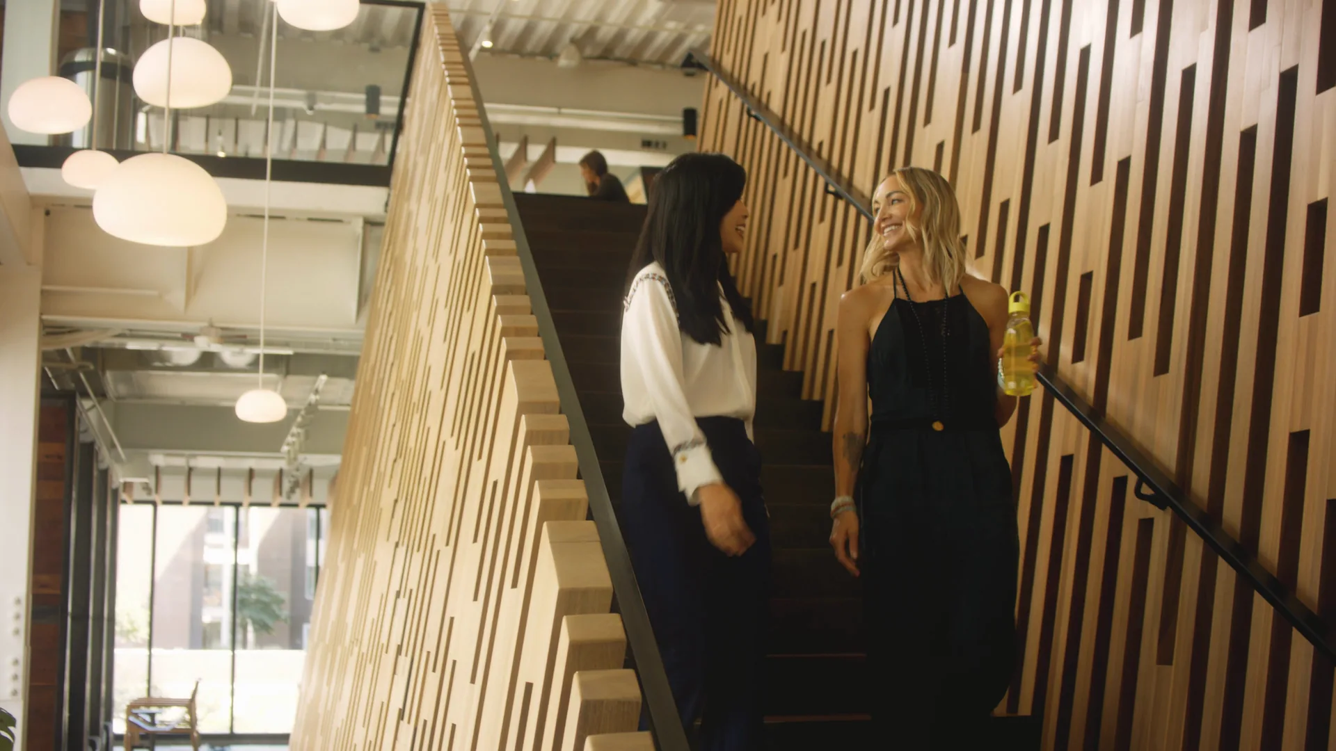 Two women walking down a wood-slatted staircase