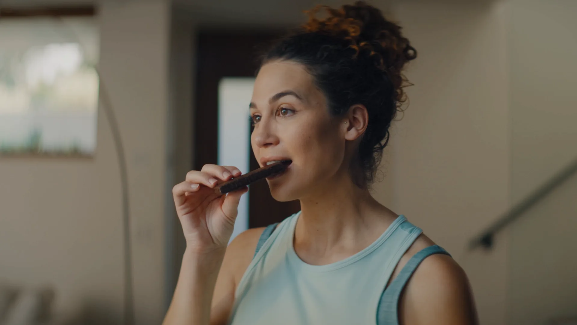 Woman taking a bite of a protein bar at home
