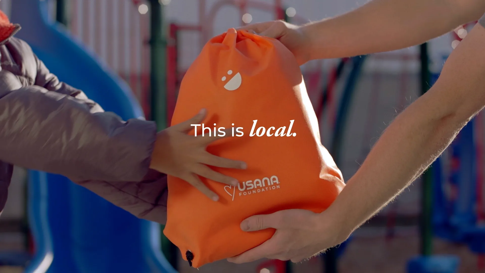 Hands passing an orange USANA bag: This is local
